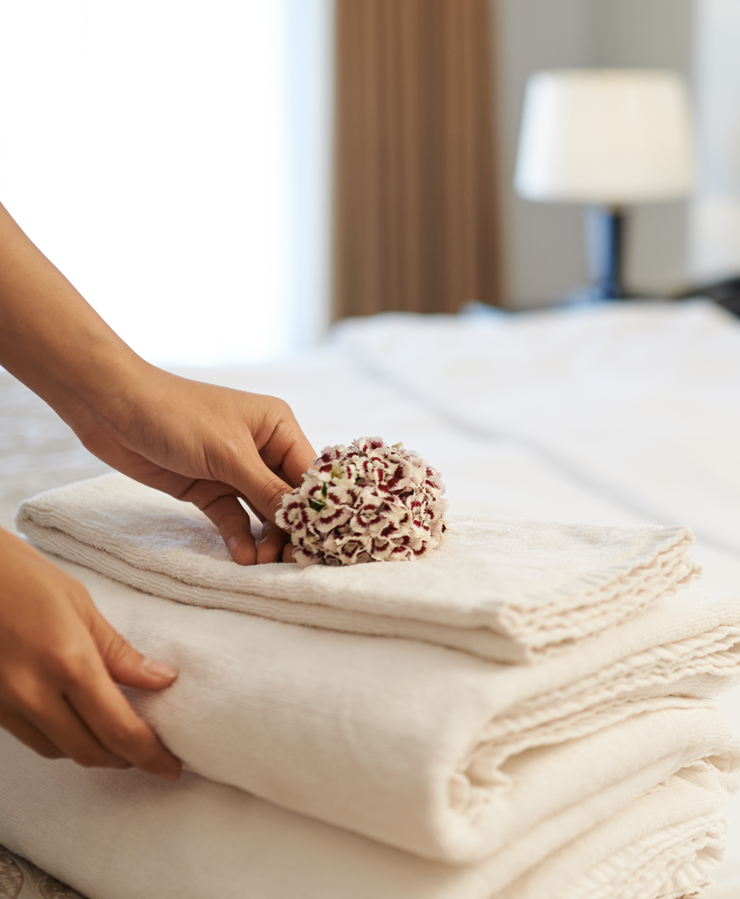 womans hands placing flower on bed linens in hotel