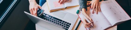 writing in notebook with laptop keyboard on desk