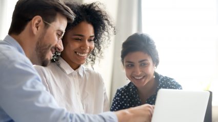 group of workers pointing to laptop in office setting