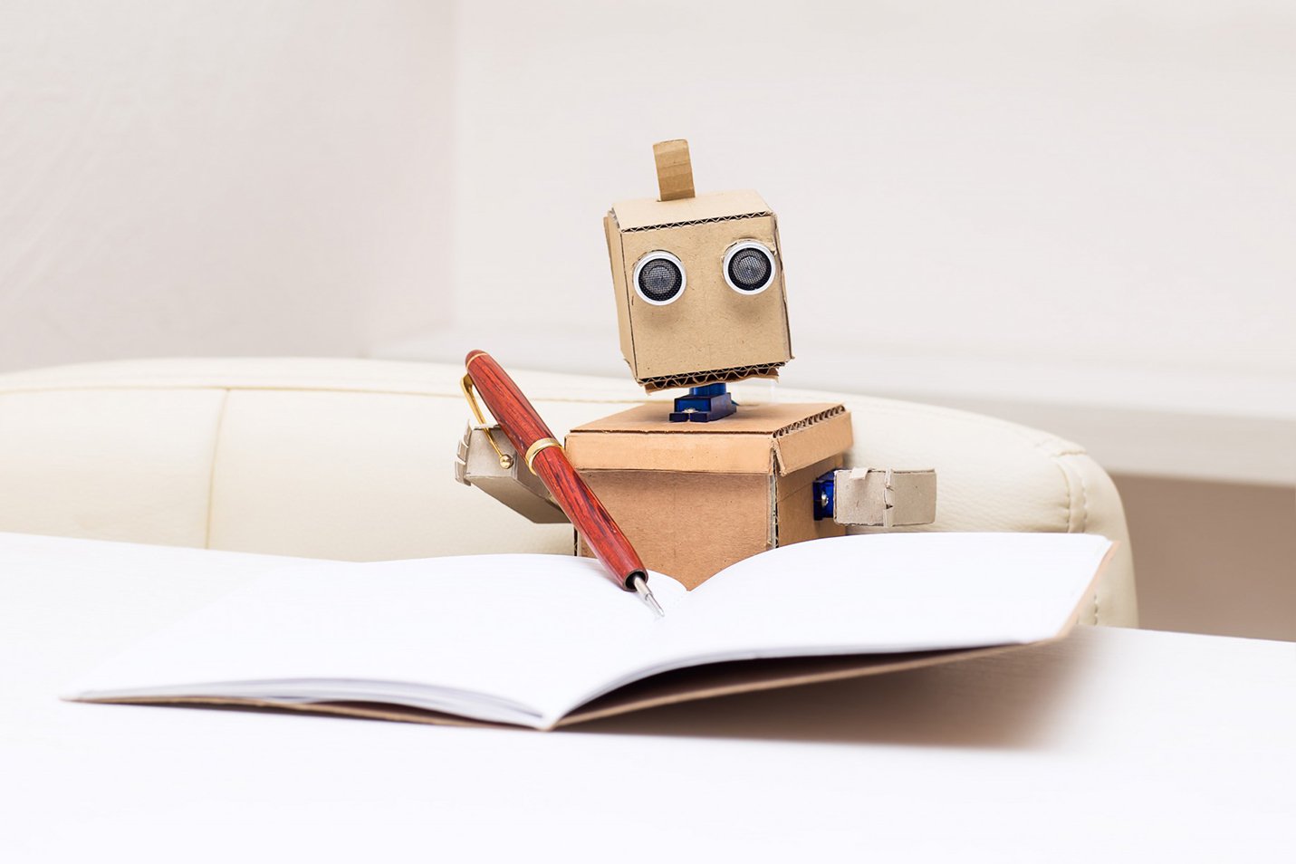 cardboard robot writing in notebook