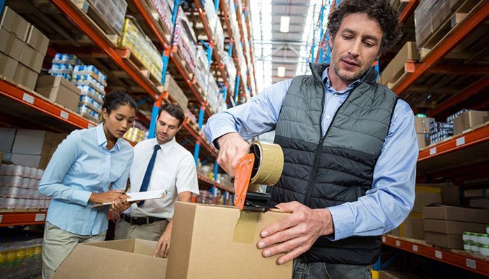 man taping cardboard box in warehouse