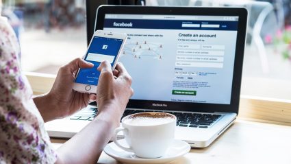 woman holding phone with facebook login screen and facebook on computer