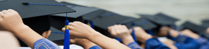 graduates in cap and gown with hands on caps