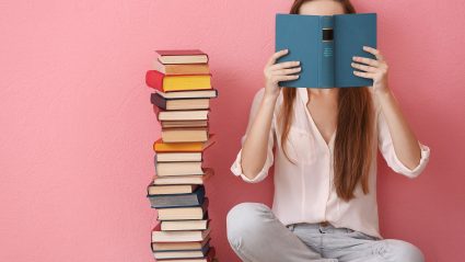 woman covering face with book on pink background
