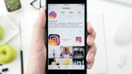 hand holding phone with instagram on screen white desk background