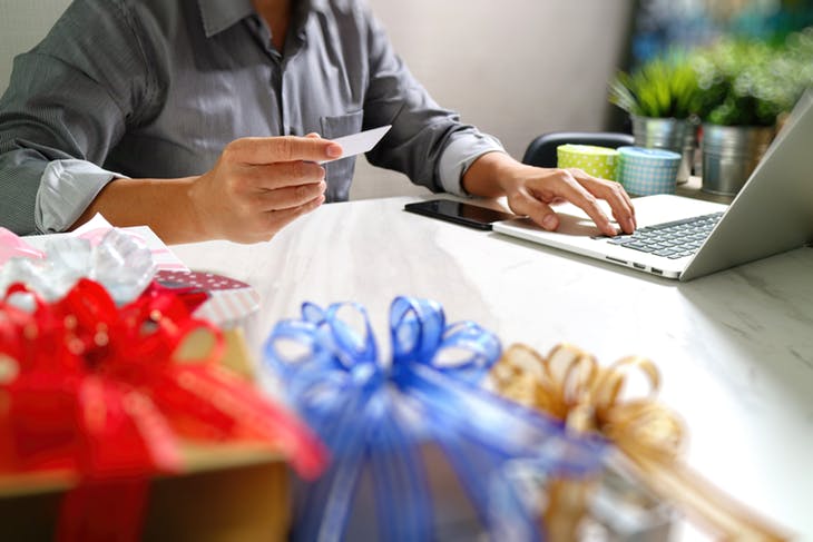 close up of man entering credit card at computer desk with gifts