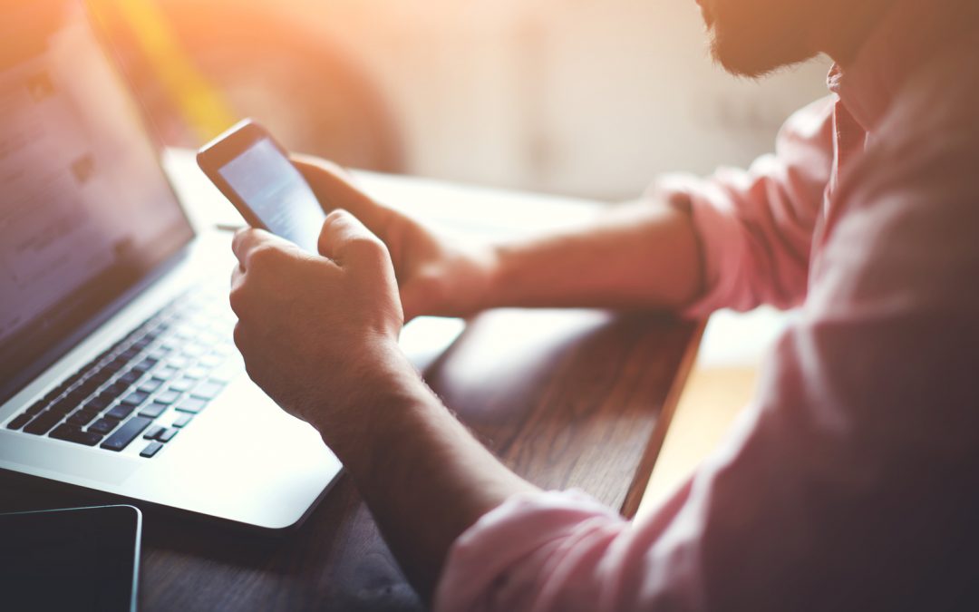 person searching on phone in front of laptop