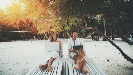 couple sitting on beach with laptops