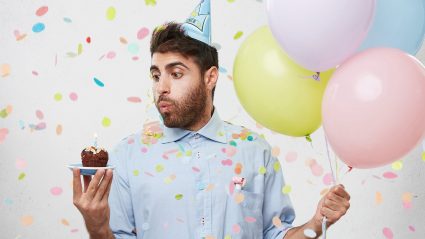 Man holding balloons and blowing out candle on birthday cupcake