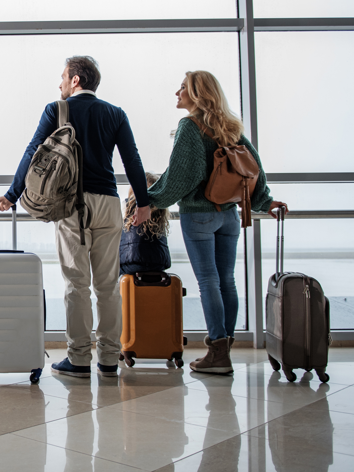 man and woman at airport with luggage looking out windows