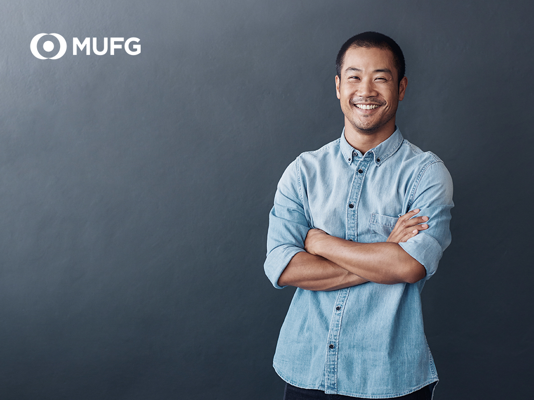asian man smiling with folded arms dark grey background