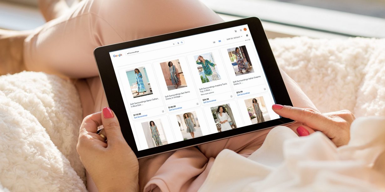 Person holding a tablet and browsing an online clothing store displaying various women's outfits and prices.
