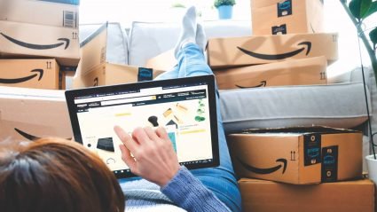 Person shopping on Amazon.com on a tablet, surrounded by Amazon boxes