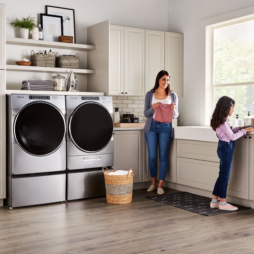 A mother and daughter fold laundry beside a Whirlpool washer and dryer