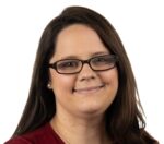 A woman with long brown hair, wearing glasses and a red top, smiles at the camera against a white background.