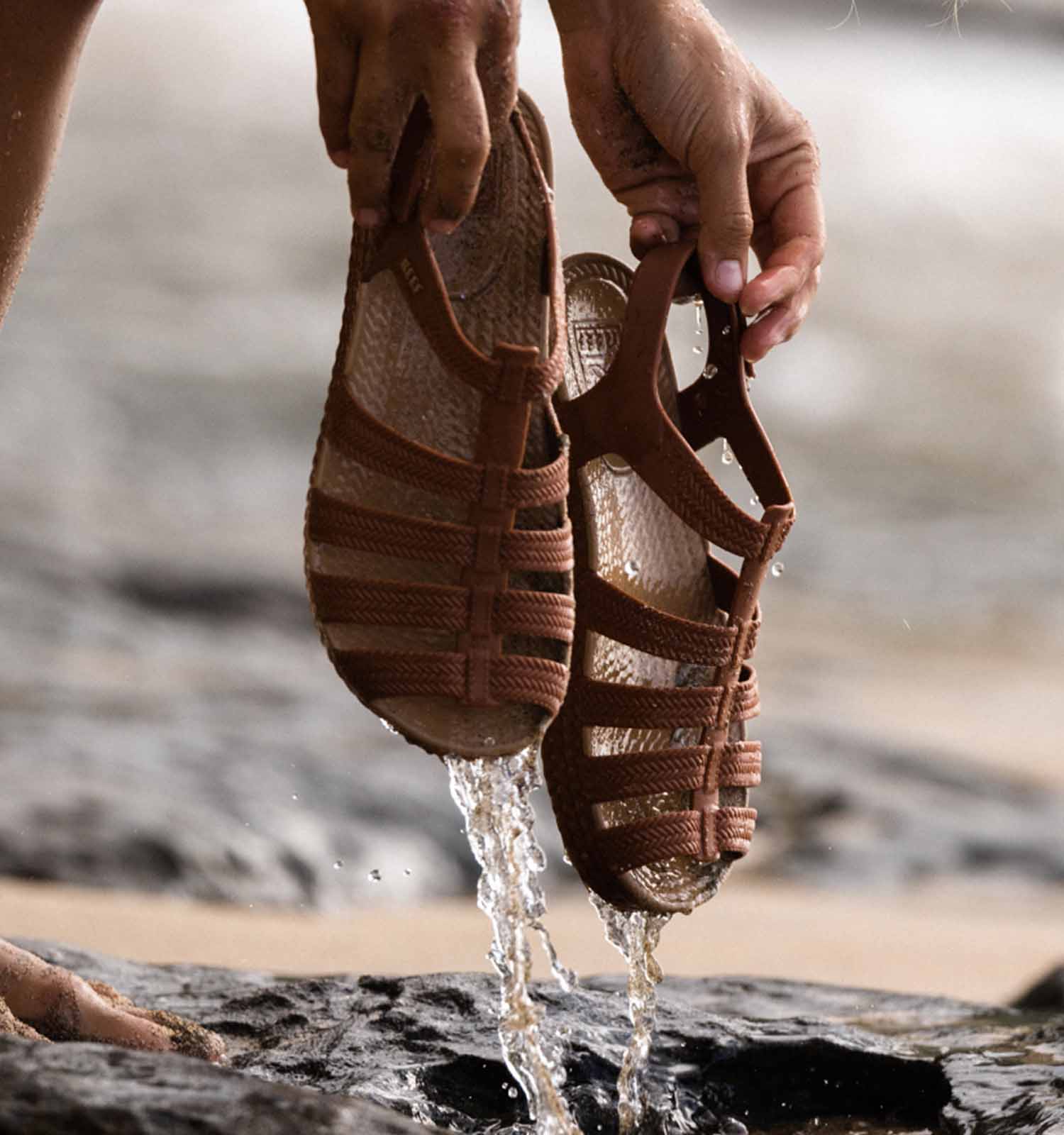 Closeup of woman's hands holding Reef brand sandals in the ocean
