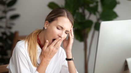 Photo of a woman yawning in front of a computer