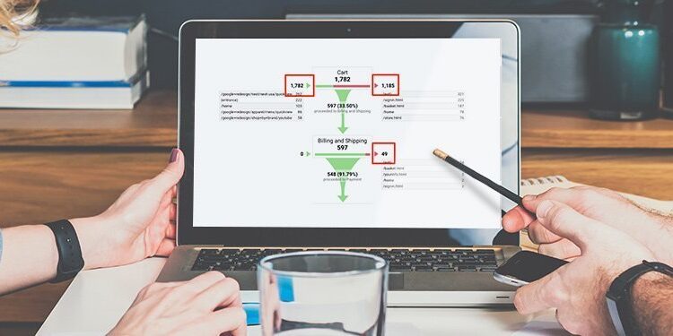Two people sitting at a desk review a flowchart displayed on a laptop screen, with one person pointing at the screen using a pencil.