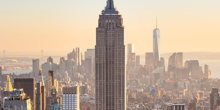 Manhattan skyline with the Empire State Building centered, seen during sunset with surrounding skyscrapers and the Hudson River in the background.