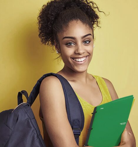 Young woman with curly hair holds green folders and wears a backpack, smiling in front of a plain yellow background.