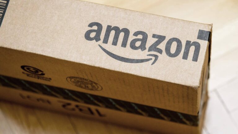 A cardboard shipping box with the Amazon logo printed on the side, placed on a wooden surface.