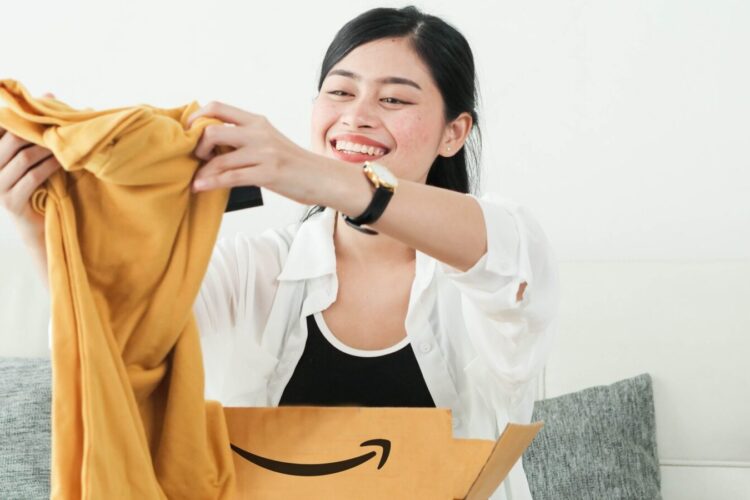A woman sits on a couch, smiling as she takes a yellow garment out of an open Amazon delivery box.
