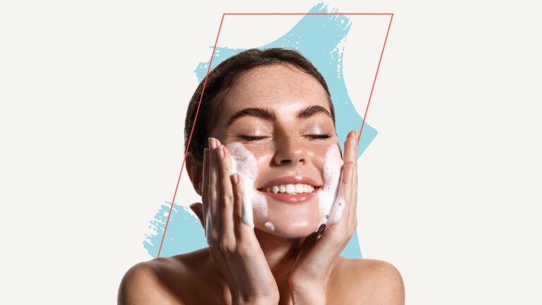 A woman with a bare shoulder smiles with closed eyes while applying foamy facial cleanser to her cheeks, against a white background with blue and pink graphic accents.
