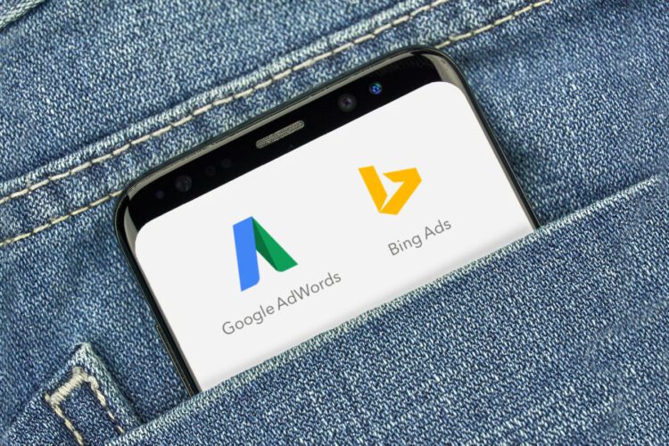 A smartphone in a denim pocket displays the Google AdWords and Bing Ads logos on its screen.