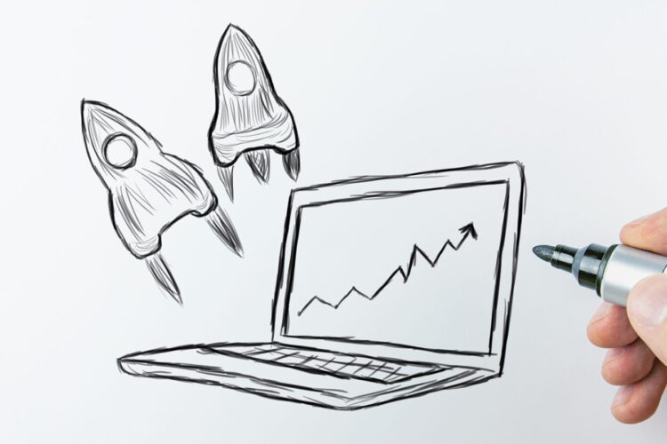 Hand draws a laptop with a rising graph on its screen and two rockets launching, symbolizing business or technology growth.