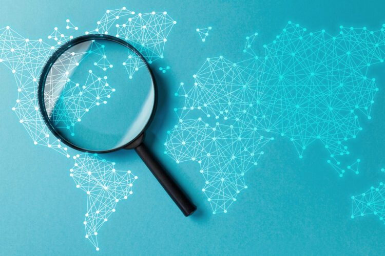 A magnifying glass placed over a blue digital world map with interconnected dots and lines, highlighting a section of the map.