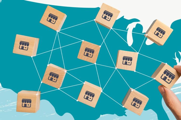 A hand connects wooden blocks with store icons over a map of the United States, illustrating a network of franchises or businesses.