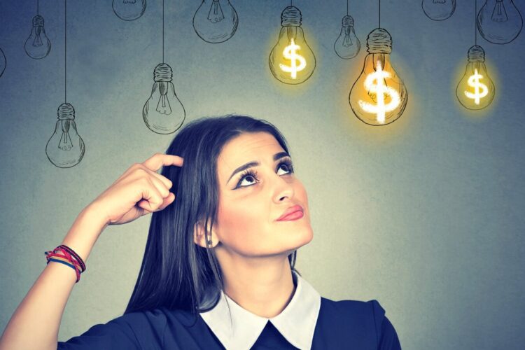A woman scratches her head and looks up at drawn light bulbs, some glowing with dollar signs inside, against a gray background.