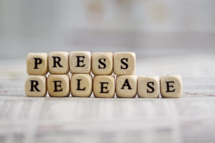 Wooden blocks arranged on a newspaper spell out "PRESS RELEASE.