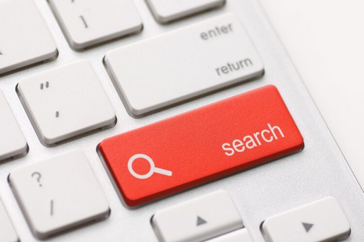 Close-up of a computer keyboard with a prominent red key labeled "search" featuring a magnifying glass icon, replacing the usual key in the position next to the "enter" key.