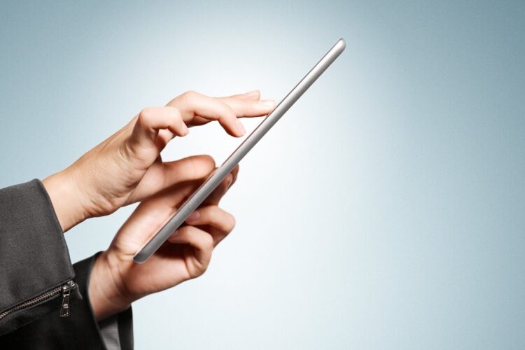 A person wearing a dark suit uses a touchscreen tablet against a light blue gradient background.