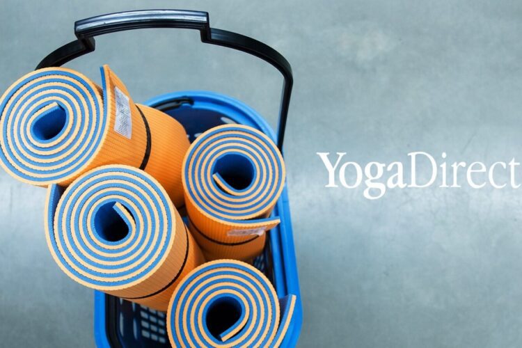 Four rolled orange and blue yoga mats in a blue basket, viewed from above, with the "YogaDirect" logo on a plain gray background.