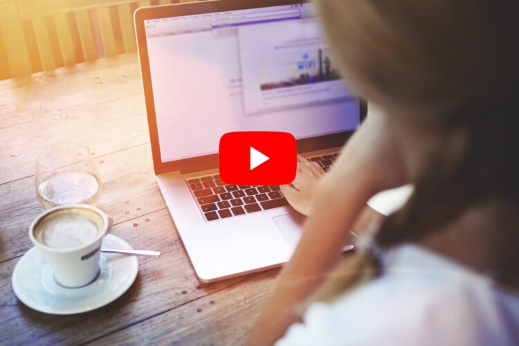 A person uses a laptop at a wooden table with a cup of coffee and juice; the laptop screen shows a blurred webpage.