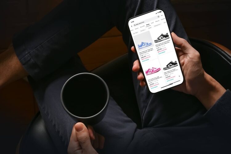 A person holding a cup and browsing sneakers on a smartphone while sitting with legs crossed.