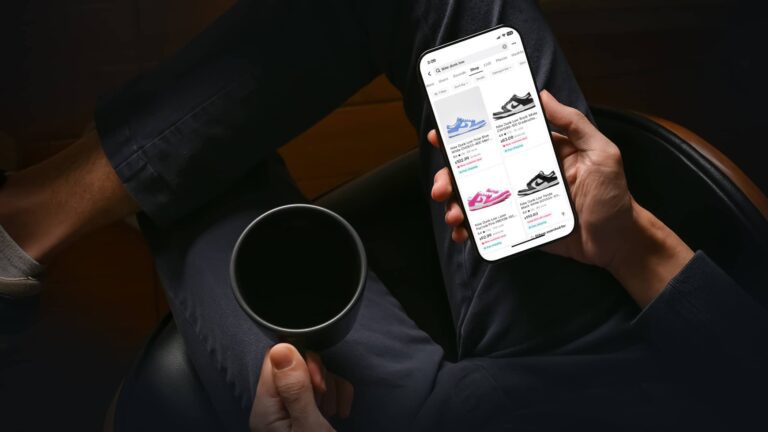 A person holding a cup and browsing sneakers on a smartphone while sitting with legs crossed.