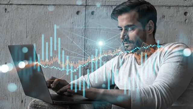 A man works on a laptop with overlaid digital graphs and data visualizations, suggesting analysis or trading activity.
