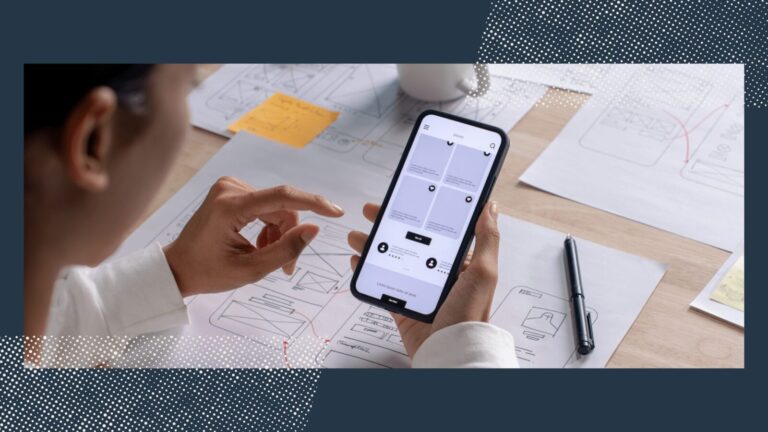 A person uses a smartphone to view a wireframe app design, with printed wireframes, a pen, and notes on a desk in the background.
