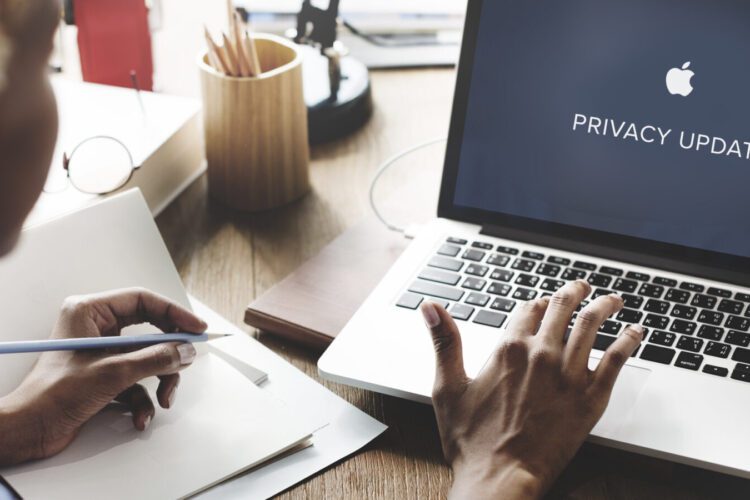 Person using a laptop displaying "PRIVACY UPDATE" on the screen, with notepad, pen, and office supplies on the desk.