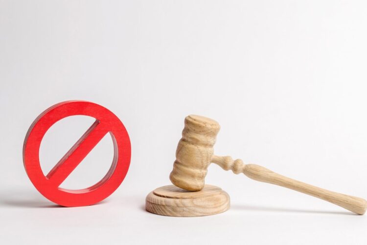 A wooden gavel rests on a sound block next to a red prohibition sign against a white background.