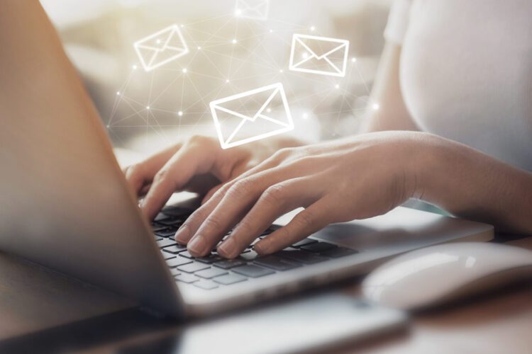 Person typing on a laptop with illustrated email icons appearing above the keyboard, suggesting digital communication or sending emails.