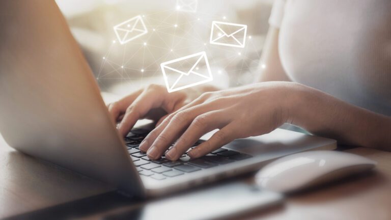 Person typing on a laptop with illustrated email icons appearing above the keyboard, suggesting digital communication or sending emails.