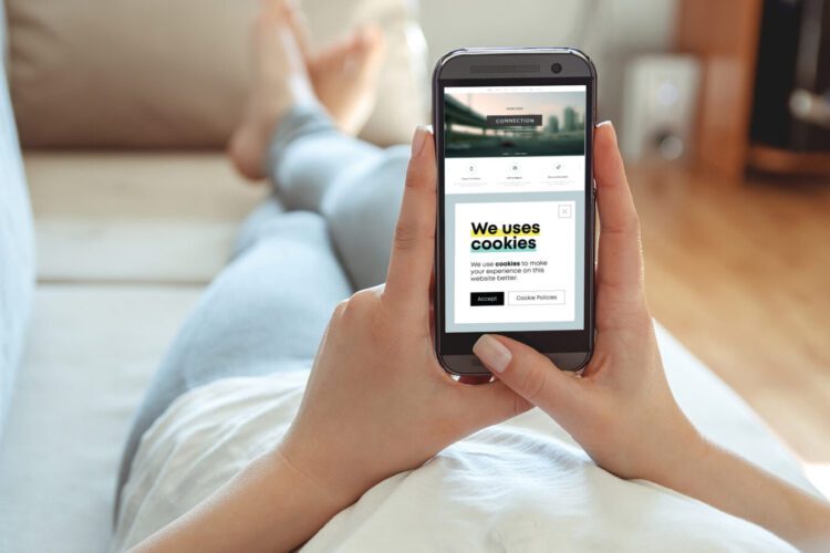 Person lying on a couch holding a smartphone, which displays a website with a cookie consent pop-up message.