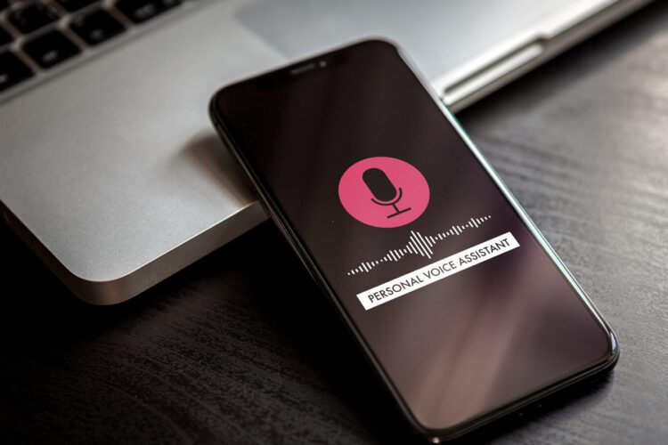 A smartphone with a personal voice assistant interface is on a dark desk next to a laptop keyboard.