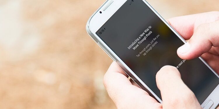 Person holding a white smartphone and typing on the screen outdoors, with a beaded bracelet and pink string bracelet visible on their wrist.