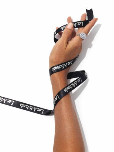 A hand with a diamond ring holds a black ribbon that reads "Lea Michele" in white script.
