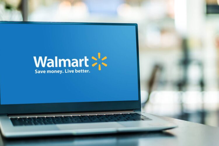 A laptop on a table displays the Walmart logo and slogan "Save money. Live better." on its screen, with a blurred indoor background.
